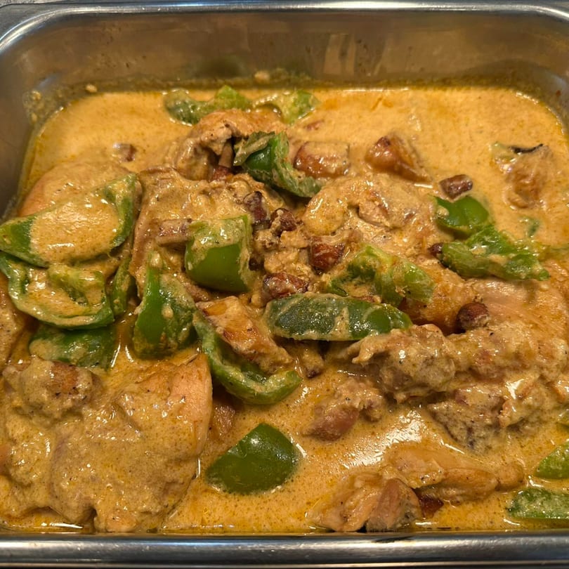 Filipino chicken adobo with green bell peppers in a creamy, savory sauce, served in a metal tray.
